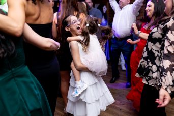 תמונה ובה ילדה בשמלה לבנה ומשקפיים מחזיקה ילדה קטנה יותר וצוחקת